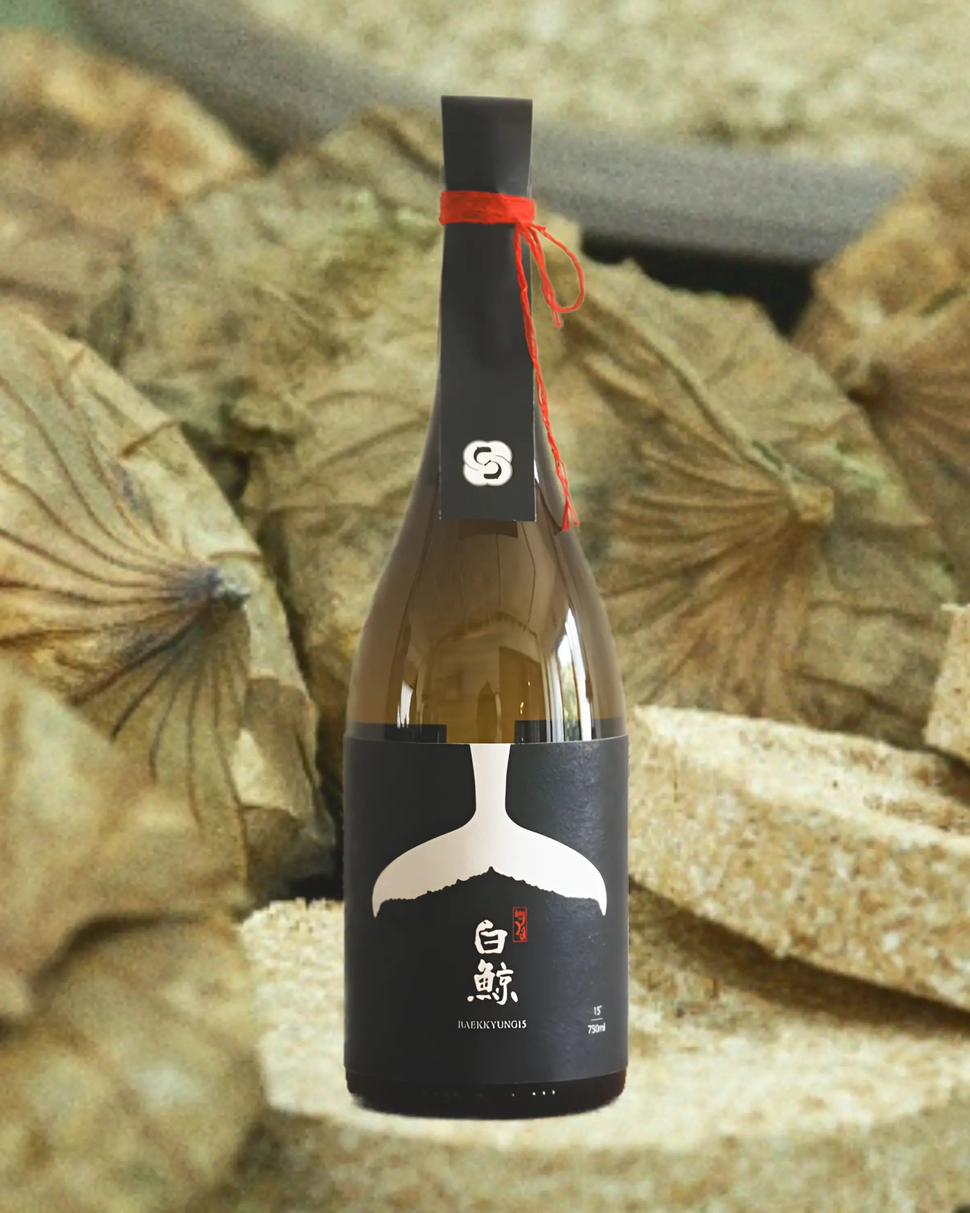 A bottle of premium Korean rice wine featuring a black paper label with a white whale tail graphic and red string, set against a background of nuruk cakes wrapped in lotus leaves. Baekkyung 15 Premium - yakju - cult