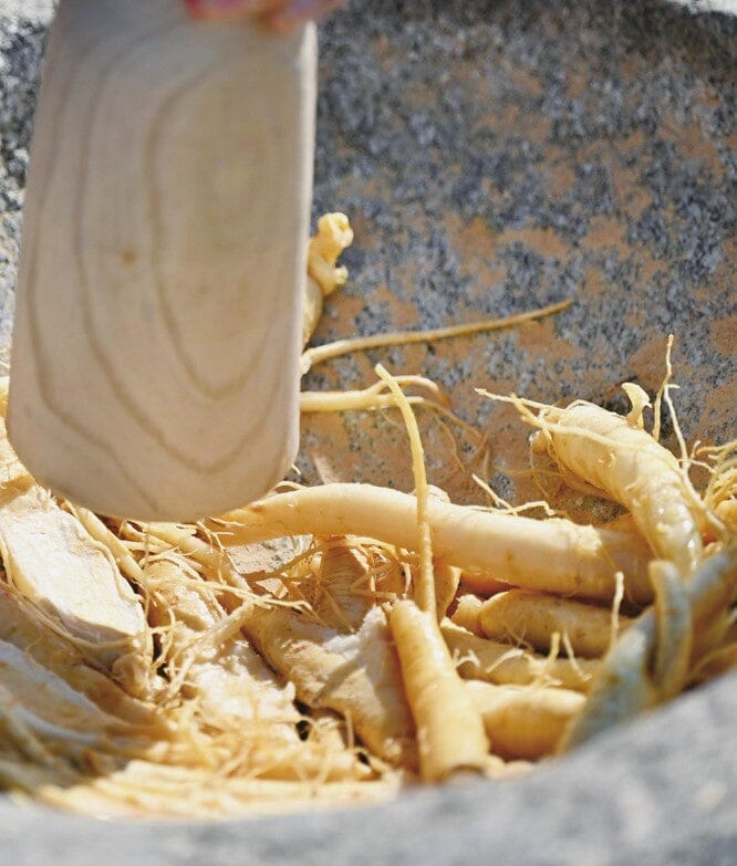 A close-up of dried or fresh ginseng roots inside a stone mortar, with a wooden pestle being used to crush or mix them.

Geumsan Ginseng Wine - Geumsan Insamju - cultsool