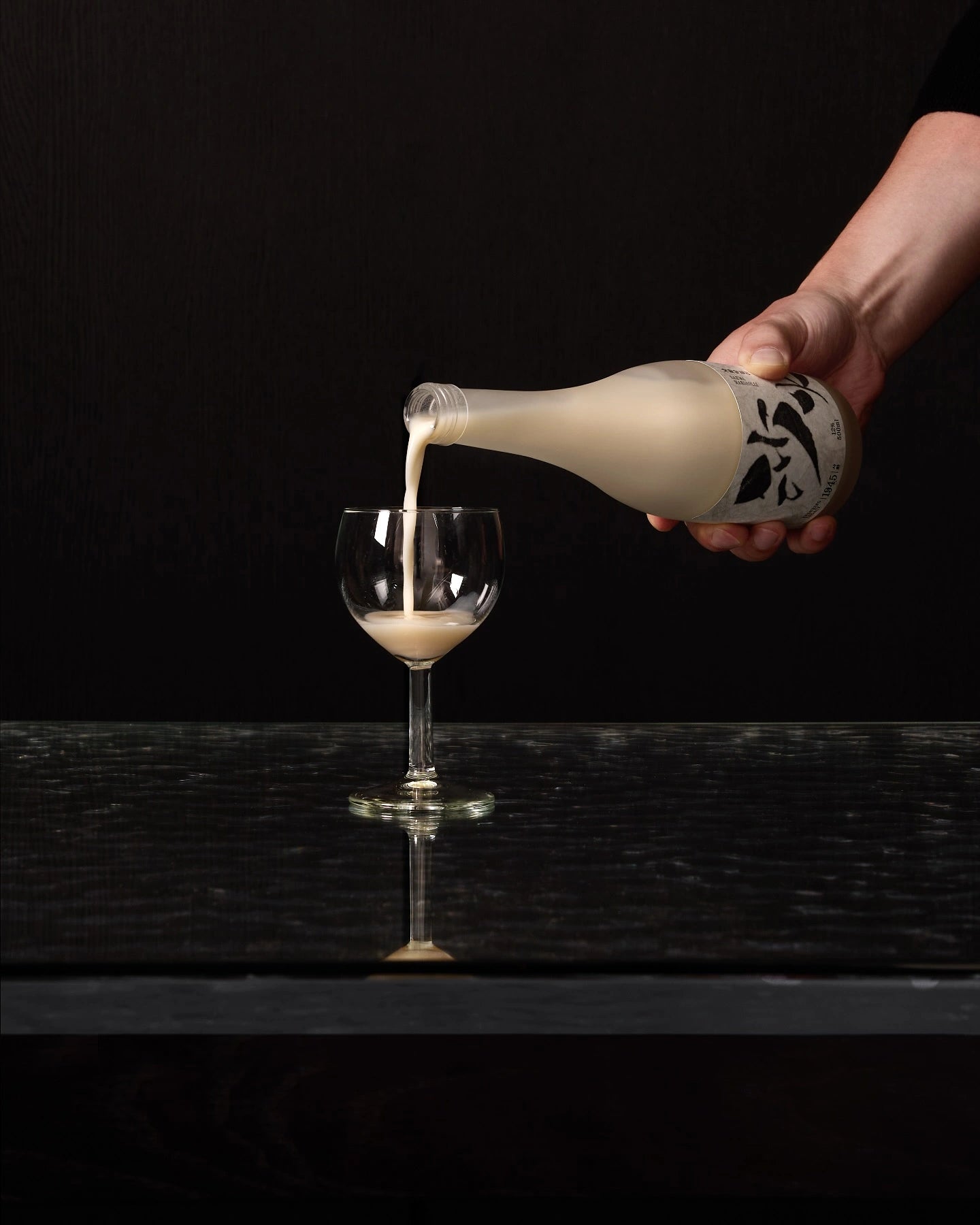 A hand pouring a creamy rice wine (makgeolli) from a traditional Korean liqyor bottle with a black graphic label into a clear stemmed glass, set against a dark background.


Sahwa Makgeolli - Good Tomorrow Brewery - cultsool