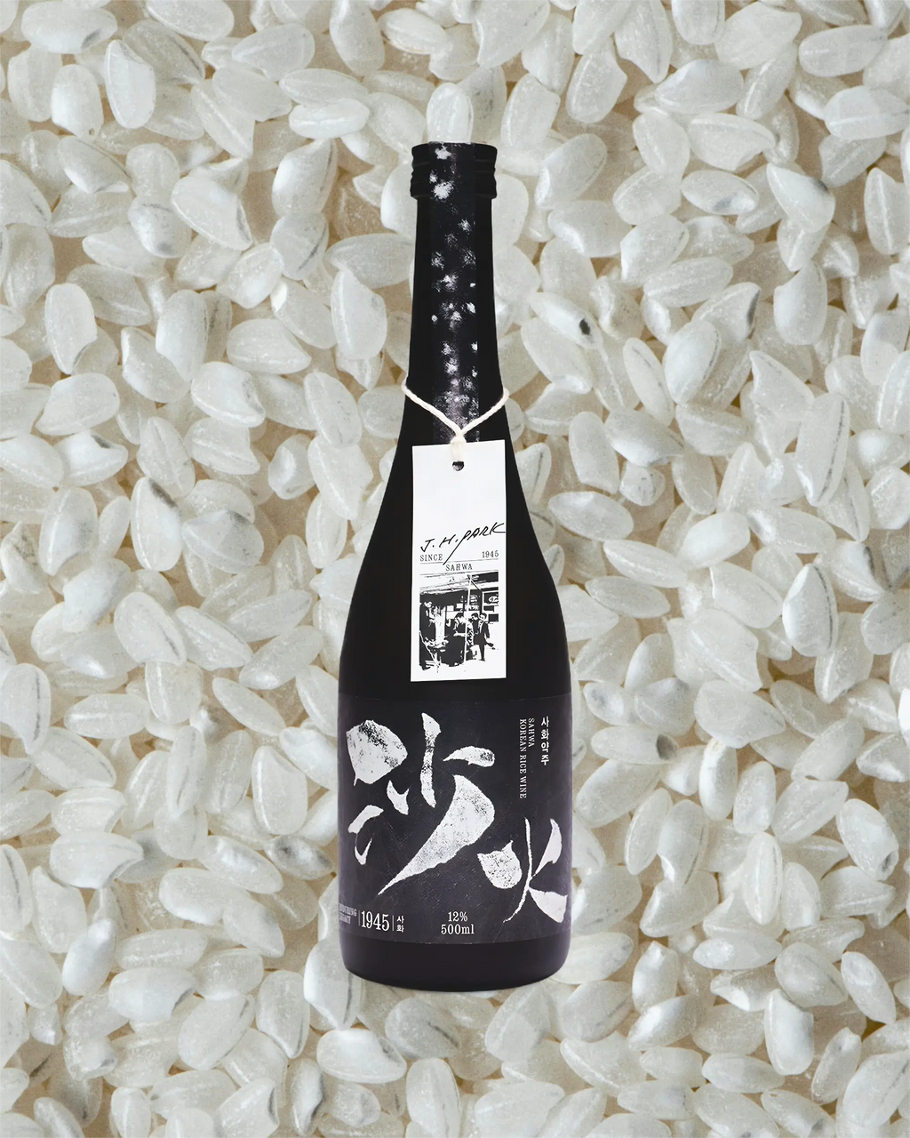 A black bottle of Korean rice wine with white calligraphy on the label on a background of white rice grains. Sahwa Yakju - Good Tomorrow Brewery - cult
