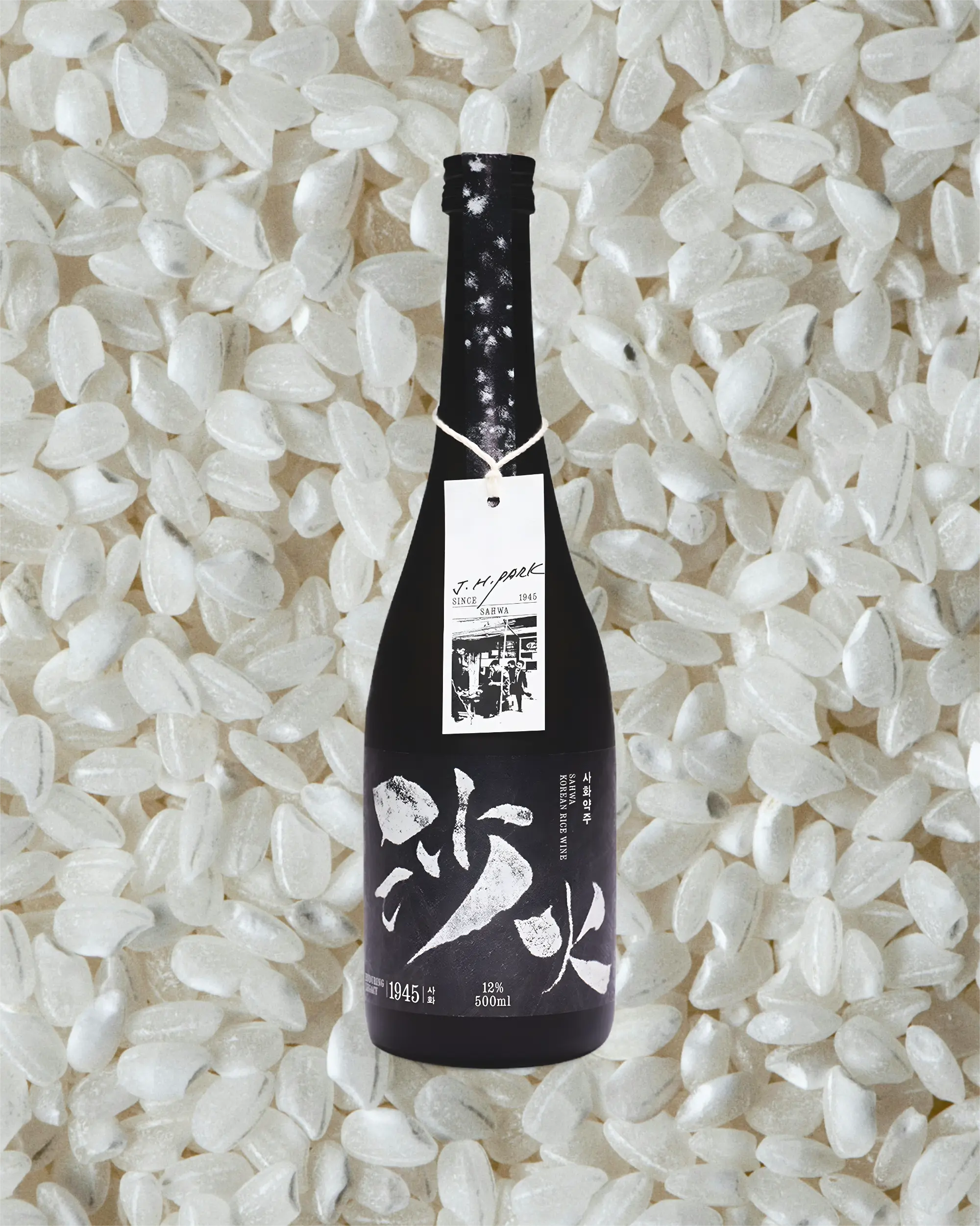 A black bottle of Korean rice wine with white calligraphy on the label on a background of white rice grains. Sahwa Yakju - Good Tomorrow Brewery - cult