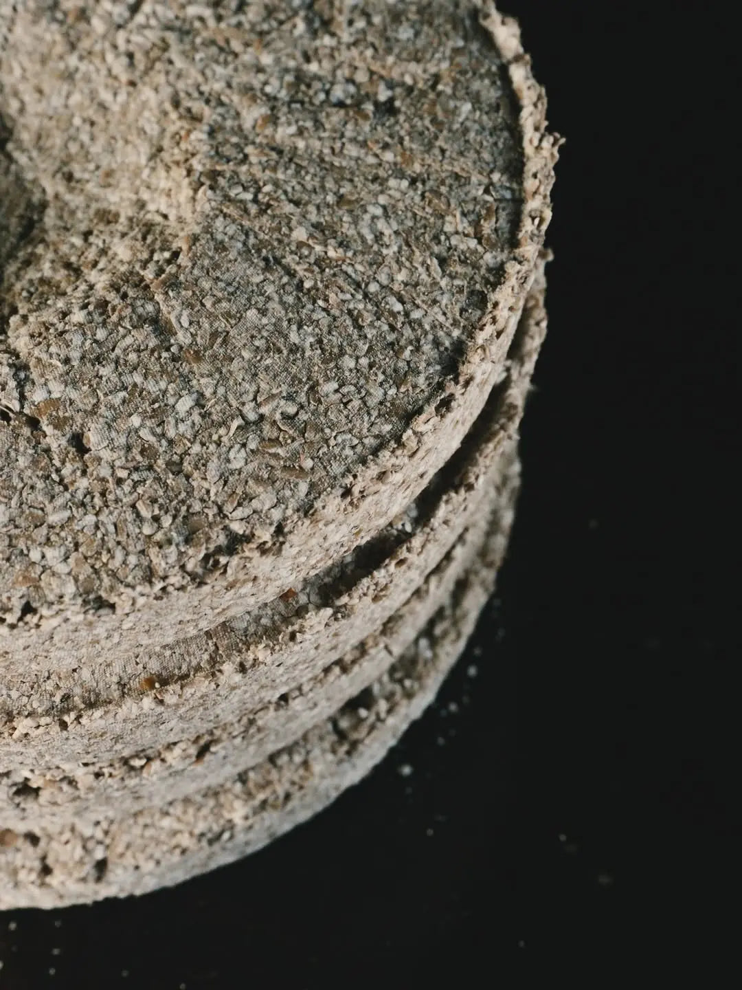 A close-up of a stack of circular nuruk cakes from Baekkyung Distillery set against a solid black background.
