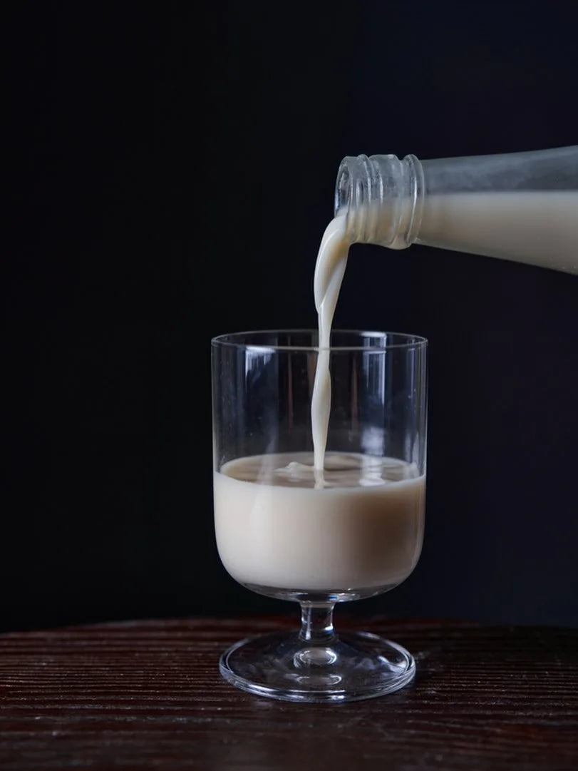 A glass bottle pouring a full bodied makgeolli into a clear stemmed glass on a dark wooden surface against a black background.

Sahwajeongmiso Makgeolli - Good Tomorrow Brewery - cultsool